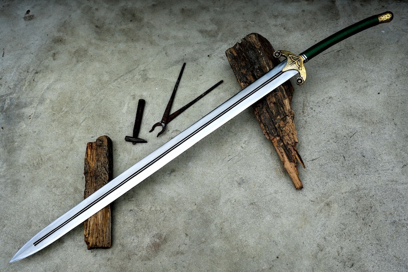 May include: A long, silver sword with a green handle and gold accents, resting on a weathered wooden surface. Blacksmith tools, including tongs and a hammer, are also visible. The sword's blade is approximately 36 inches long.
