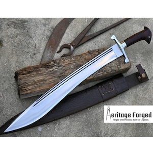 May include: A large, polished steel sword with a brown handle and a leather sheath. The blade has three black stripes. The sword is lying on a wooden plank with other tools in the background. The text "Aeritage Forged" is visible.