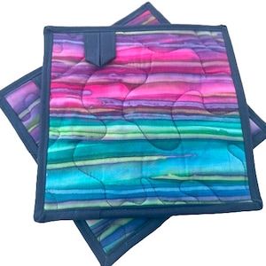 May include: Two quilted hot pads with a colorful striped pattern in shades of pink, purple, blue, and green. The hot pads have a dark blue border.