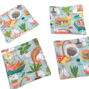 May include: Set of four blue and green fabric coasters with a whimsical cat theme. Each coaster features a different cat design with various colors and patterns. The coasters are perfect for protecting surfaces from heat and spills.