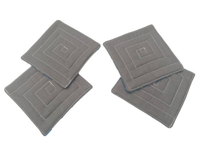 May include: Four gray quilted fabric coasters with a white geometric design. The coasters are stacked on top of each other.