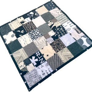 May include: A black and white patchwork quilt with a black border. The quilt is made of various fabrics with different patterns, including stars, stripes, and polka dots. The quilt is approximately 12 inches by 12 inches.