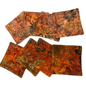May include: Set of eight orange and brown fabric coasters with a floral pattern. The coasters are made of a soft, quilted fabric and have a subtle sheen.