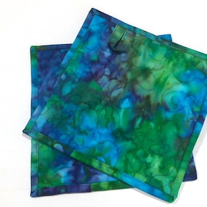 May include: Two blue and green quilted pot holders with a tie-dye pattern. The pot holders have a dark blue border.