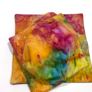 May include: A set of two tie-dye bowl cozies and a matching square hot pad. The fabric features a vibrant mix of yellow, orange, pink, and blue hues. The cozies are quilted with black thread, and the hot pad is square.