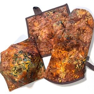 May include: Set of three brown and green floral patterned kitchen pot holders. The set includes a large oven mitt, a smaller pot holder, and a square hot pad.
