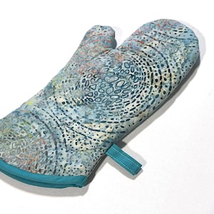 May include: A teal blue oven mitt with a colorful abstract pattern. The mitt has a loop for hanging.