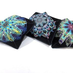 May include: Three black square pot holders with colorful, intricate mandala designs. The mandalas feature shades of blue, yellow, purple, and pink. The pot holders are made of fabric and have a quilted appearance.