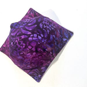 May include: Purple and blue fabric bowl with a floral pattern. The bowl is made of cotton and is perfect for holding small items.