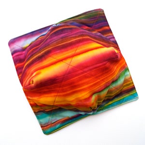 May include: A colorful fabric bowl with a striped pattern in shades of red, orange, yellow, green, and blue. The bowl is folded and appears to be made of quilted fabric.