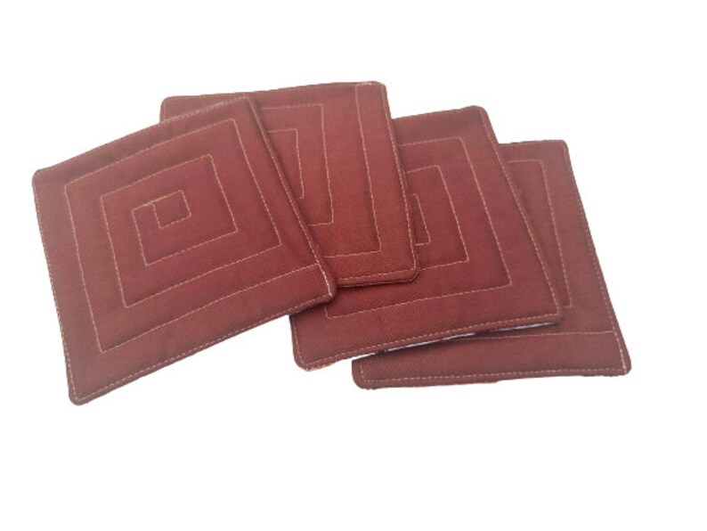 May include: Set of four brown quilted fabric coasters with a square design. Each coaster has a white stitched border and a square pattern in the center.