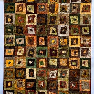 May include: A rectangular quilt featuring a grid of square blocks, each containing an off-center, irregularly shaped quadrilateral patch. The fabric displays a variety of earth-toned patterns in shades of brown, green, gold, and cream.