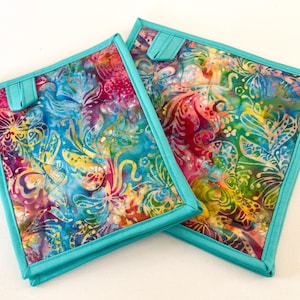 May include: Two turquoise quilted hot pads with a colourful floral pattern. The fabric features a batik design with shades of pink, blue, yellow, and green.