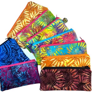 Peut inclure: Un ensemble de huit pochettes zippées colorées avec des motifs en tissu batik. Les pochettes sont disposées en éventail, la plus grande en haut et la plus petite en bas. Les pochettes sont faites de différents tissus, dont du bleu, de l'orange, du rose et du violet.