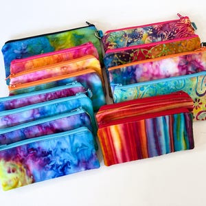 May include: A collection of 12 colorful zippered pouches with tie-dye patterns. The pouches are made of fabric and have a variety of colors, including blue, red, orange, yellow, and green.