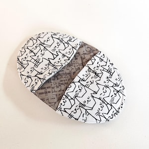 May include: A white fabric pouch with a black and white cat print. The pouch is open and the inside is lined with a gray fabric.