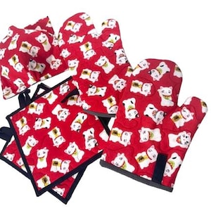 May include: Set of red oven mitts and pot holders with a white lucky cat pattern. The mitts and holders have black trim.