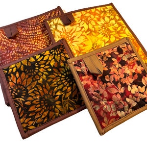 May include: Four quilted pot holders with different floral patterns in shades of red, orange, yellow, and brown. The pot holders have brown fabric trim and a loop handle.