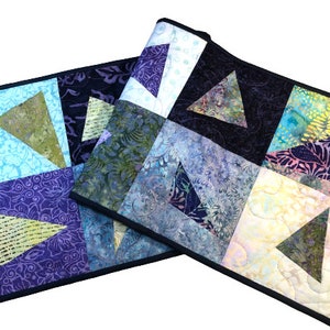 May include: Two quilted table runners featuring a geometric pattern of triangles in shades of blue, green, purple, and yellow. The fabric has a batik design.
