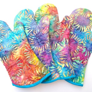 May include: Set of four colorful oven mitts with a blue trim. The mitts feature a quilted design with a repeating pattern of colorful flowers.