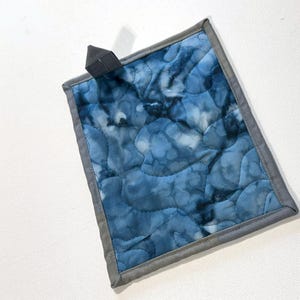 May include: A blue quilted hot pad with a gray border. The hot pad has a tie-dye pattern and is perfect for protecting surfaces from hot dishes.
