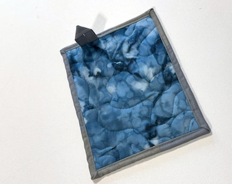 May include: A blue quilted hot pad with a gray border. The hot pad has a tie-dye pattern and is perfect for protecting surfaces from hot dishes.