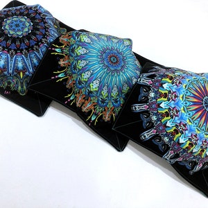 May include: Three black fabric bowls with colorful mandala designs. The bowls are lined up in a row on a white surface.
