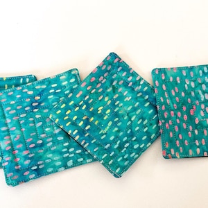May include: Four teal blue fabric coasters with a white and pink polka dot pattern. The coasters are quilted and have a subtle sheen.