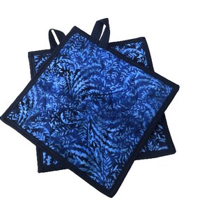 May include: Two blue and black pot holders with a blue floral pattern. The pot holders have a loop handle.