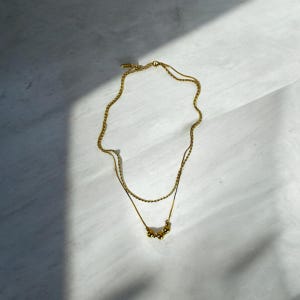 May include: A gold layered necklace with a delicate chain and a pendant of small gold beads.