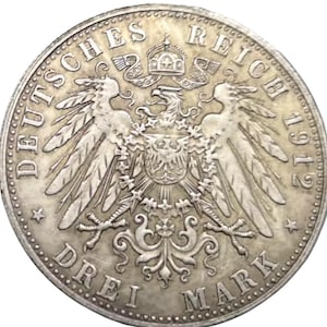 May include: A silver coin from 1912 featuring the German Imperial Eagle with outstretched wings, a crown, and the text "DEUTSCHES REICH" and "DREI MARK". The coin has a detailed design and a circular shape.