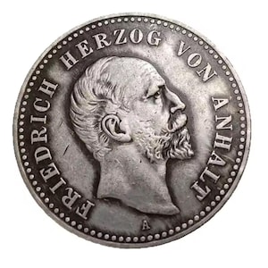 May include: A silver coin featuring a profile of a man with a beard, surrounded by text. The coin's edge has a dotted pattern. The text includes "FRIEDRICH" and "HERZOG VON ANHALT".