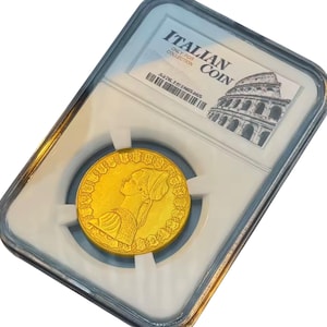 Op de afbeelding: Een gouden Italiaanse munt in een doorzichtige plastic houder. De munt toont een profiel van een vrouw en is gemarkeerd met "ITALIAN COIN" met een afbeelding van het Colosseum. De houder is gelabeld "ONLY FOR COLLECTION".