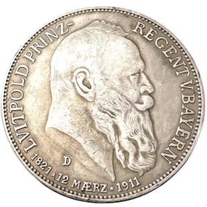 May include: A silver coin featuring a profile of a man with a long beard. The coin has text around the edge, including the words "LUITPOLD PRINZ" and "REGENT V. BAYERN", along with the date "1821" and "1911".