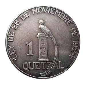 May include: A silver coin featuring a quetzal bird perched on a column, with the number 1 and the word "QUETZAL" below. The coin's edge is inscribed with text, including "LEY DE 26 DE NOVIEMBRE DE 1924".