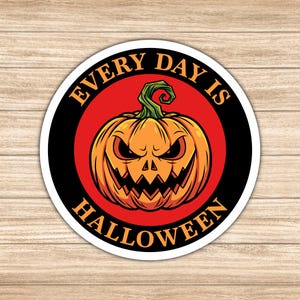 May include: A round sticker with a cartoon jack-o'-lantern design. The pumpkin is orange with a green stem and a menacing carved face. The text "EVERY DAY IS HALLOWEEN" is in a circular pattern around the pumpkin, with a red background and black border.
