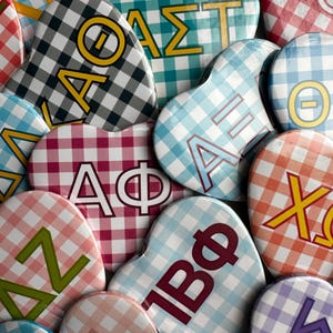 Könnte beinhalten: Eine Sammlung herzförmiger Knöpfe mit verschiedenen griechischen Buchstaben und Mustern. Die Knöpfe sind in verschiedenen Farben, darunter rosa, blau, rot und weiß. Die Buchstaben sind in verschiedenen Schriftarten und Größen.
