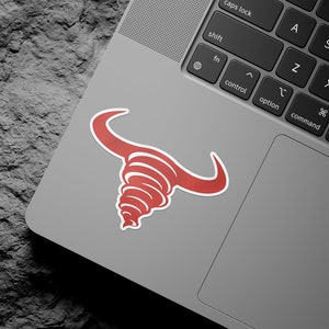 Peut inclure: Autocollant de taureau rouge sur un ordinateur portable argenté. Le taureau est stylisé avec un motif en spirale.