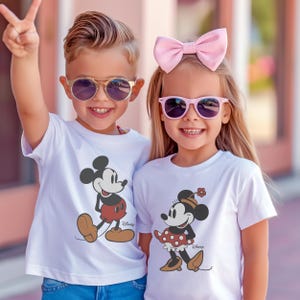 May include: Two children wearing white t-shirts with Mickey and Minnie Mouse graphics. The boy wears gold-rimmed sunglasses and the girl wears pink sunglasses and a pink bow. The boy is holding up two fingers.