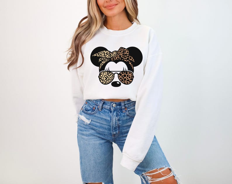 May include: White sweatshirt featuring a graphic of a cartoon mouse with a leopard print bow, sunglasses, and ears. The mouse graphic is in black and tan. The sweatshirt has long sleeves and a crew neck.