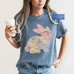 Puede incluir: Una camiseta azul con un diseño de conejo de patchwork. El conejo tiene orejas de cuadros rosas, un lazo de encaje y un cuerpo con estampado floral. El texto "FAUX PATCHWORK DTF PRINT" está en un recuadro azul.