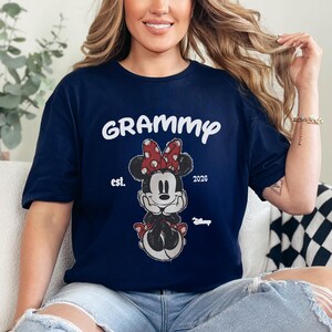 K&ouml;nnte beinhalten: Marineblaues T-Shirt mit dem Wort "Grammy" in wei&szlig;er Schrift &uuml;ber einer Minnie Mouse-Grafik. Die Grafik enth&auml;lt eine rote gepunktete Schleife und den Text "est. 2026". Unten befindet sich ein Disney-Logo.