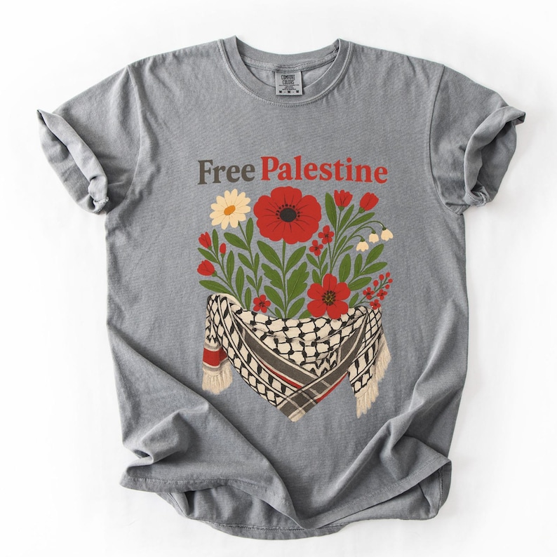 May include: Gray t-shirt with the text "Free Palestine" in brown and red. The shirt features a floral design with red poppies, white flowers, and a keffiyeh scarf.
