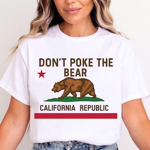May include: White t-shirt with the text "DON'T POKE THE BEAR" above a brown bear graphic on green grass. Below the bear is the text "CALIFORNIA REPUBLIC" with a red stripe at the bottom. A red star is to the left of the text.