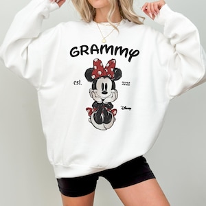 K&ouml;nnte beinhalten: Wei&szlig;es Sweatshirt mit dem Wort "Grammy" in schwarzer Schrift &uuml;ber einer Minnie Mouse-Grafik. Die Grafik enth&auml;lt eine rote Schleife mit wei&szlig;en Punkten, den Text "est. 2026" und das Disney-Logo.