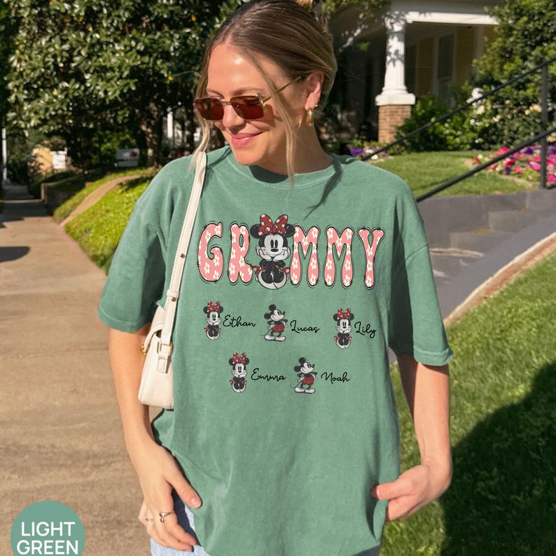 May include: Light green t-shirt with the word "Grammy" in pink floral letters and a Minnie Mouse graphic. Below the word are six Minnie Mouse graphics with names: Ethan, Lucas, Lily, Emma, and Noah.