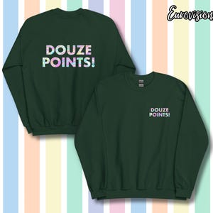 Op de afbeelding: Twee donkergroene sweatshirts met de tekst "DOUZE POINTS!" in een kleurrijk, iriserend lettertype. Eén sweatshirt heeft de tekst gecentreerd op de voorkant, de andere heeft de tekst op de linkerborst.