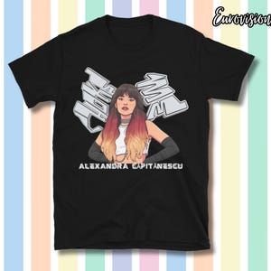 Op de afbeelding: Zwart T-shirt met een gestileerde illustratie van een vrouw met ombre haar en de tekst "Alexandra Capitanescu". Het ontwerp bevat de tekst "MAL" in een graffiti-stijl. Het shirt heeft korte mouwen.