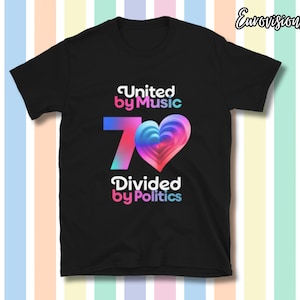 Op de afbeelding: Zwart T-shirt met de tekst "United by Music" boven een kleurrijk hart en het getal "70". Onder het hart staat de tekst "Divided by Politics". De achtergrond heeft gekleurde strepen.