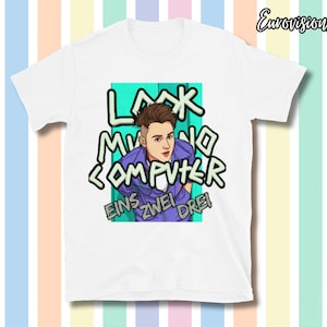 Op de afbeelding: Wit t-shirt met een cartoon illustratie van een persoon in een paarse jas. Het shirt toont de woorden "LOOK NO COMPUTER" en "EINS ZWEI DREI" in een gestileerd lettertype. De achtergrond is gestreept met pastelkleuren.